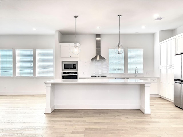 7705 Westside Villas Ln, Houston, TX 77055 - kitchen featuring light wood-style floors, light countertops, wall chimney exhaust hood, white cabinetry, and appliances with stainless steel finishes