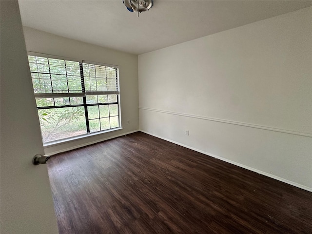 spare room with baseboards and dark wood-type flooring