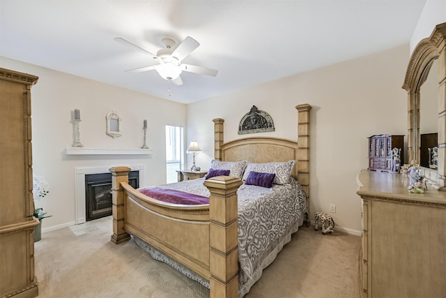 bedroom with ceiling fan, light colored carpet, a glass covered fireplace, and baseboards