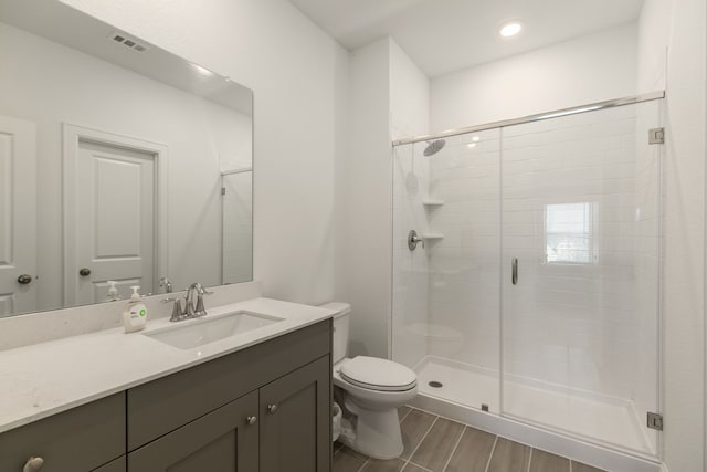 full bath with vanity, toilet, a shower stall, wood finished floors, and visible vents