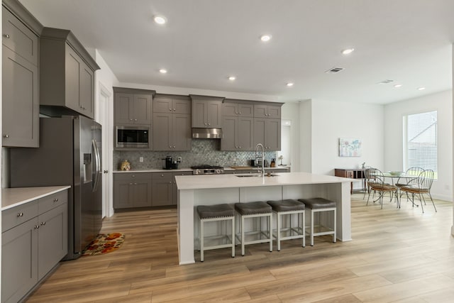 kitchen with gray cabinetry, stainless steel appliances, under cabinet range hood, and a sink