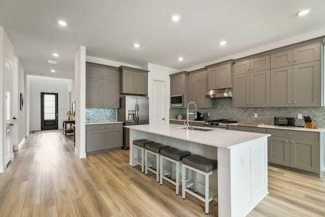 kitchen featuring a kitchen breakfast bar, under cabinet range hood, a sink, appliances with stainless steel finishes, and gray cabinetry