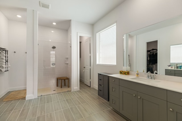 bathroom with a walk in closet, visible vents, walk in shower, vanity, and baseboards