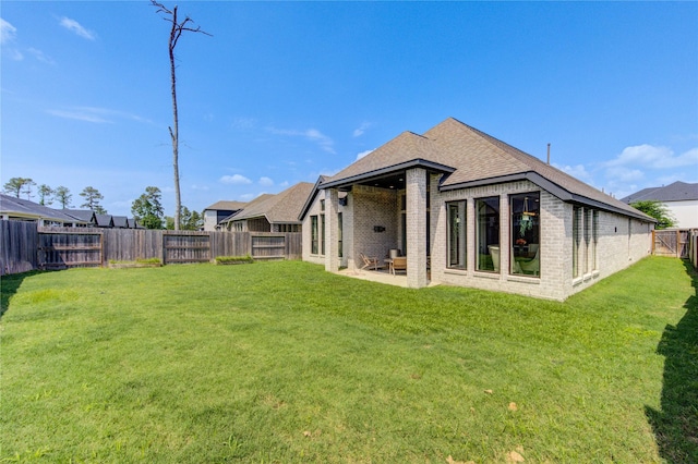 rear view of house with a yard, a shingled roof, brick siding, and a fenced backyard