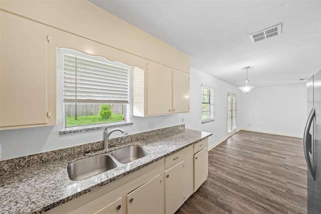 kitchen with visible vents, light stone countertops, dark wood finished floors, a sink, and stainless steel fridge