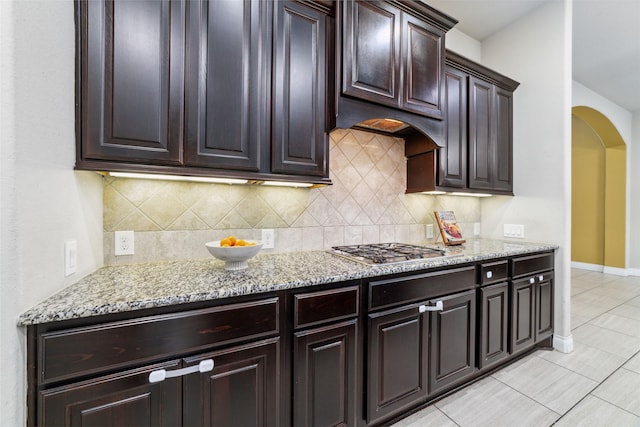 11143 Dunstan Hill Dr, Richmond, TX 77407 - kitchen with arched walkways, stainless steel gas cooktop, light stone countertops, and decorative backsplash