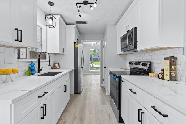 kitchen featuring visible vents, white cabinetry, a sink, light wood finished floors, and appliances with stainless steel finishes