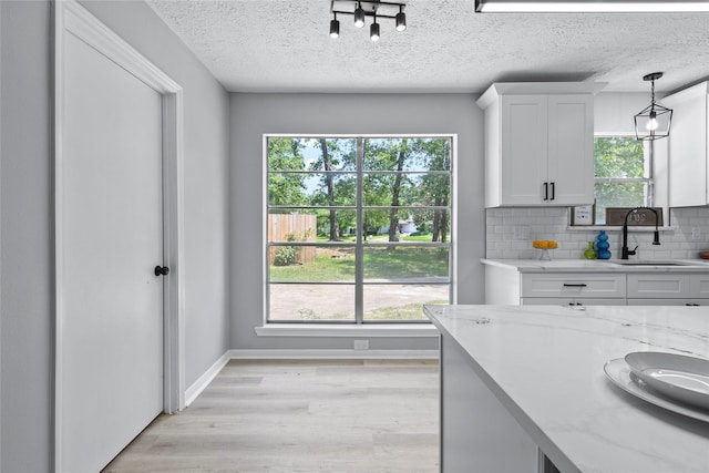 kitchen featuring a sink, light wood finished floors, a textured ceiling, white cabinetry, and tasteful backsplash