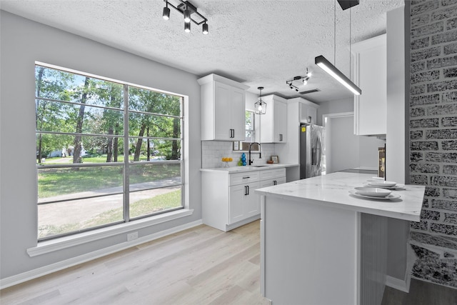 kitchen featuring decorative backsplash, stainless steel refrigerator with ice dispenser, white cabinetry, a sink, and light wood-style flooring