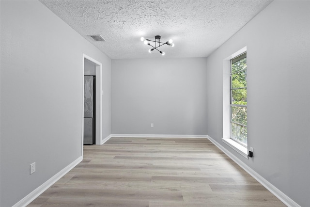 empty room with visible vents, a textured ceiling, wood finished floors, and a notable chandelier