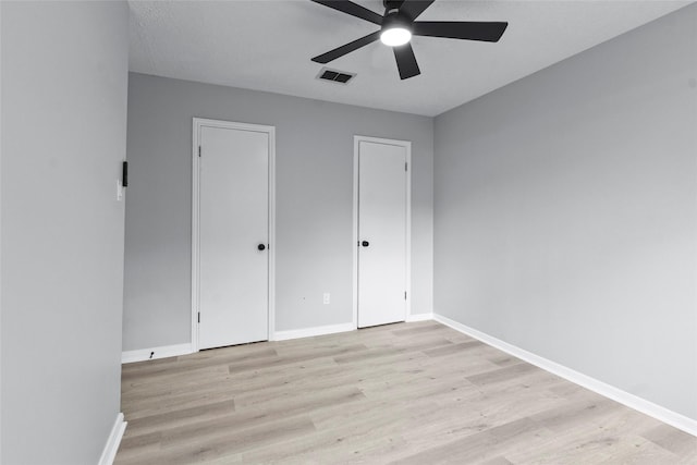 unfurnished bedroom featuring light wood-style floors, baseboards, two closets, and visible vents
