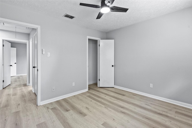 unfurnished bedroom featuring attic access, a textured ceiling, visible vents, baseboards, and light wood finished floors