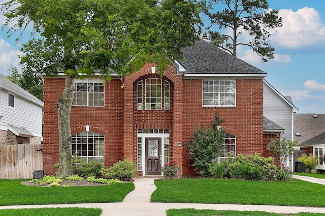 view of front of house featuring brick siding, central AC, fence, and a front yard