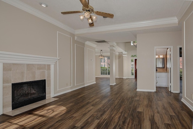 unfurnished living room featuring ornamental molding, a ceiling fan, a tile fireplace, ornate columns, and dark wood-style floors