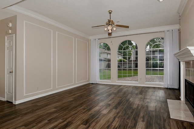 unfurnished living room with a ceiling fan, a tiled fireplace, crown molding, wood finished floors, and a decorative wall