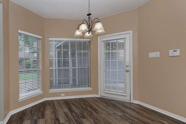 unfurnished dining area featuring an inviting chandelier, dark wood finished floors, and baseboards