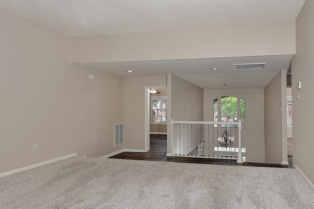 empty room with visible vents, a textured ceiling, and dark carpet