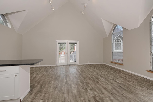 unfurnished living room featuring baseboards, rail lighting, wood finished floors, and high vaulted ceiling