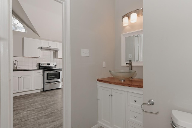 bathroom with decorative backsplash, vaulted ceiling, wood finished floors, vanity, and toilet
