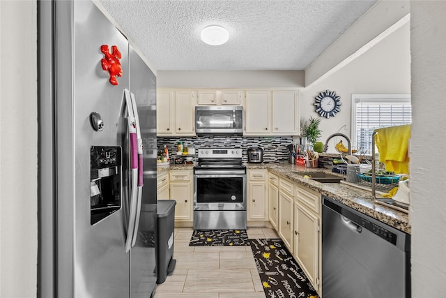 kitchen with a sink, a textured ceiling, appliances with stainless steel finishes, and backsplash