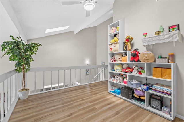 recreation room featuring lofted ceiling with skylight, wood finished floors, and ceiling fan