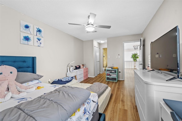 bedroom with a textured ceiling, ceiling fan, and light wood finished floors