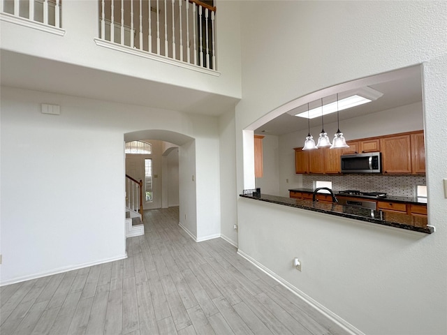 5310 Flagridge Ln, Houston, TX 77066 - kitchen with stainless steel microwave, brown cabinetry, arched walkways, a towering ceiling, and light wood-style flooring