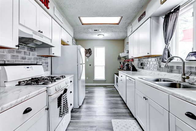 kitchen featuring visible vents, a sink, under cabinet range hood, white appliances, and white cabinetry