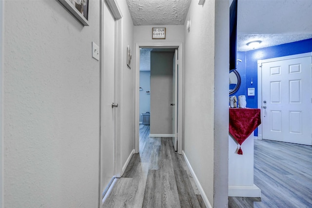 corridor featuring baseboards, a textured ceiling, and wood finished floors