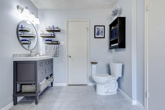 bathroom with vanity, toilet, baseboards, a textured ceiling, and tile patterned floors