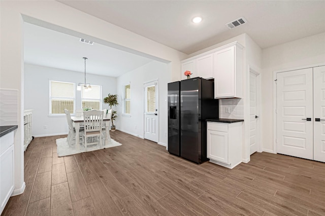 kitchen featuring dark countertops, black fridge with ice dispenser, wood finished floors, and visible vents