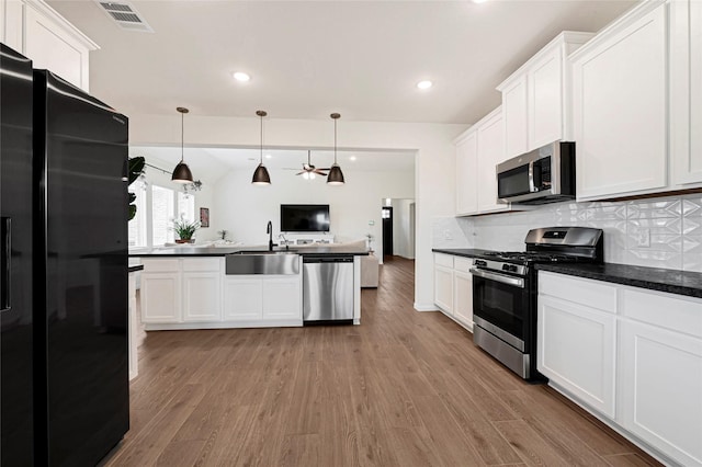kitchen with visible vents, dark countertops, a sink, open floor plan, and stainless steel appliances