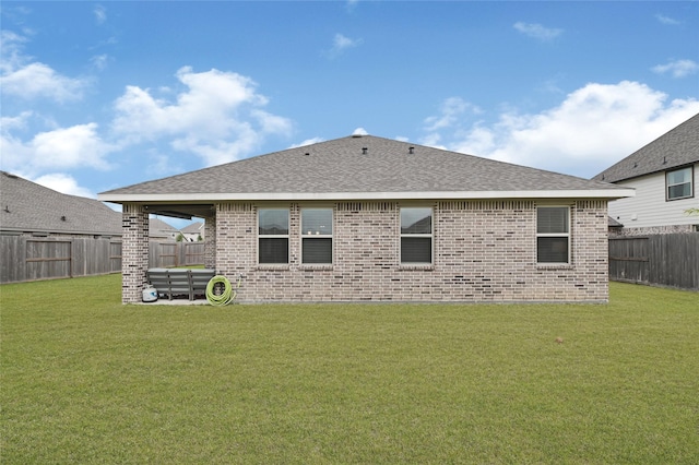 back of property with a fenced backyard, a yard, roof with shingles, and brick siding
