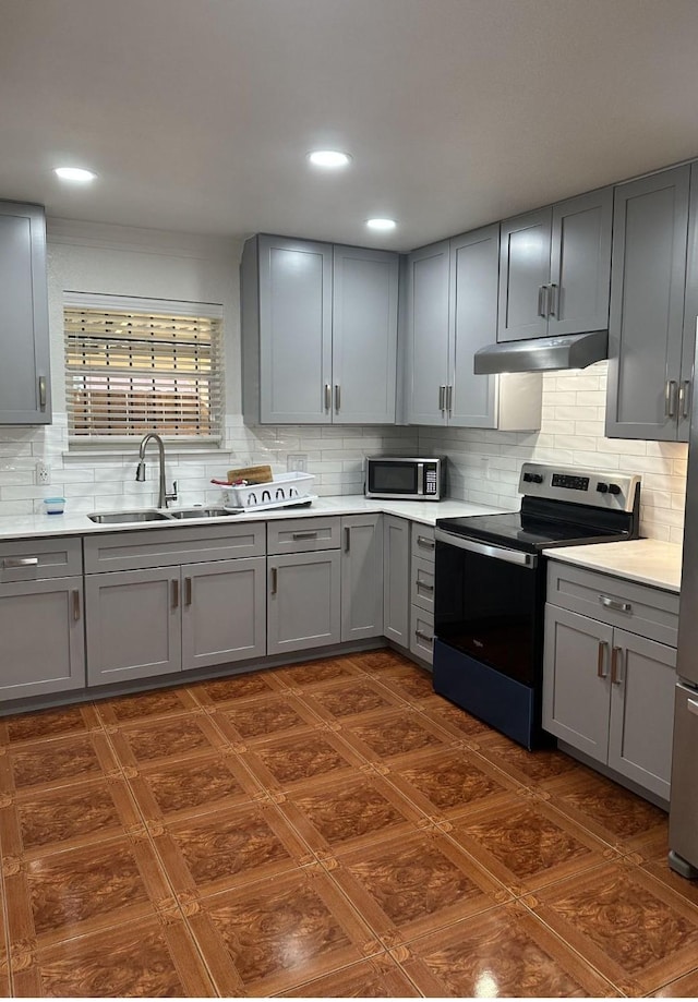 kitchen with a sink, light countertops, gray cabinets, stainless steel appliances, and under cabinet range hood