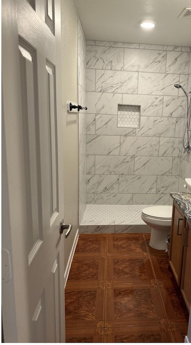 full bathroom with visible vents, a tile shower, wood finished floors, vanity, and toilet