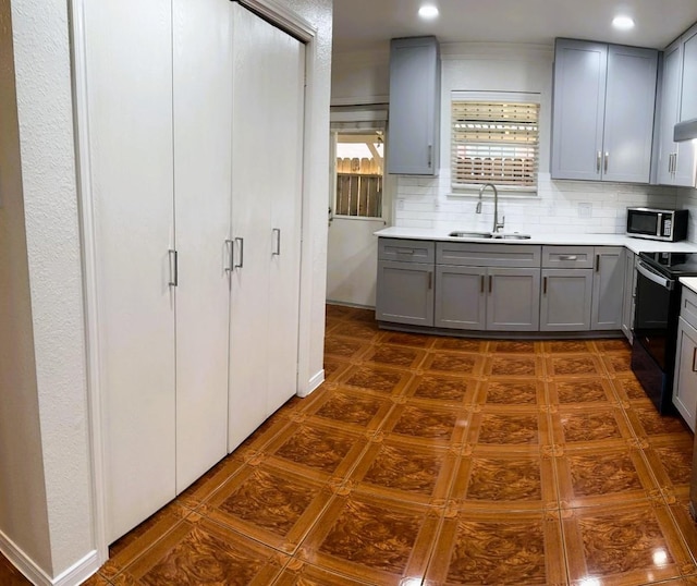 kitchen with light countertops, stainless steel microwave, black range with electric stovetop, a sink, and gray cabinetry