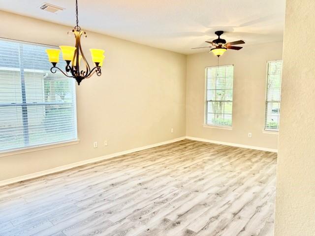 spare room featuring visible vents, baseboards, ceiling fan with notable chandelier, and wood finished floors