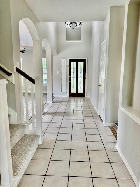 entrance foyer with light tile patterned floors, arched walkways, and stairs