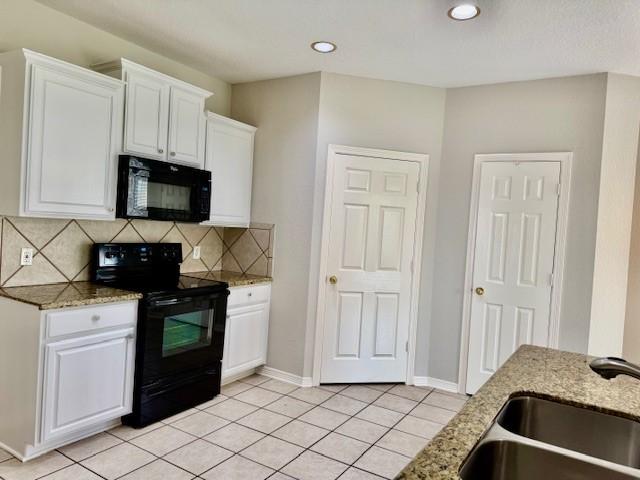 kitchen with white cabinets, light tile patterned flooring, a sink, backsplash, and black appliances