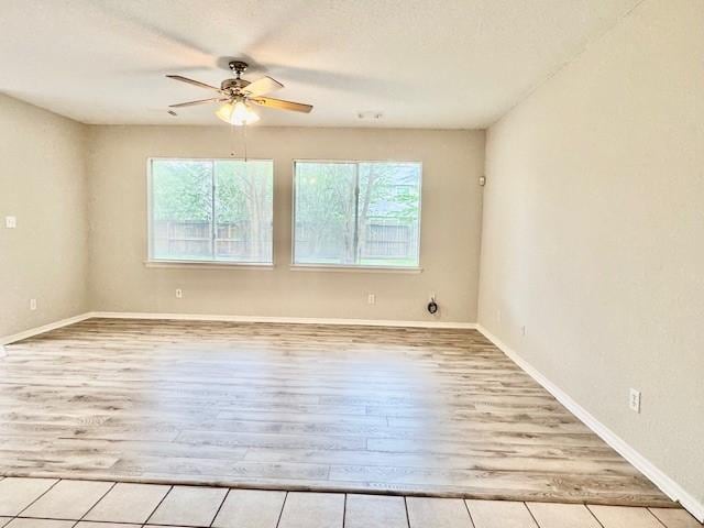unfurnished room with baseboards, a ceiling fan, wood finished floors, and a wealth of natural light