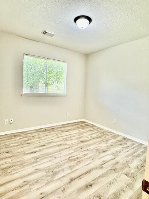 spare room featuring wood finished floors, baseboards, a textured ceiling, and visible vents