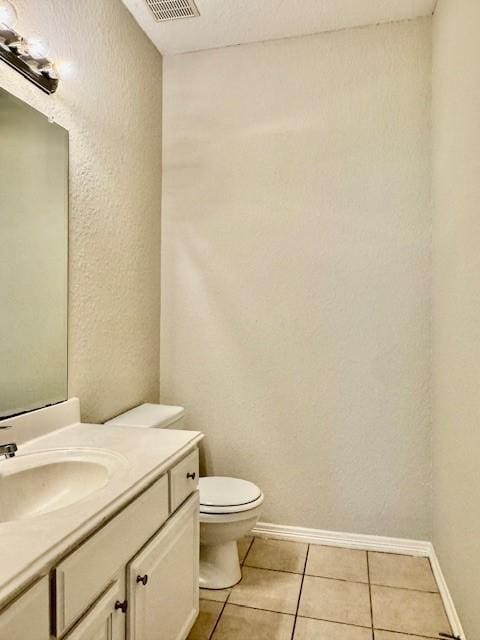half bath featuring tile patterned flooring, baseboards, vanity, toilet, and a textured wall
