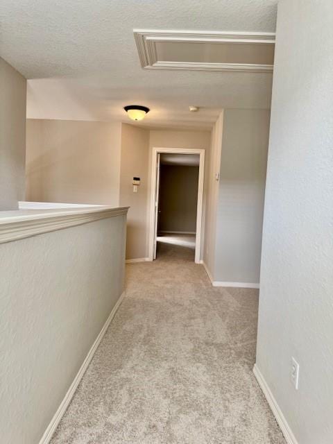corridor featuring baseboards, carpet, attic access, and a textured ceiling