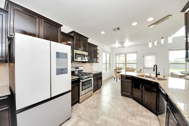 kitchen featuring appliances with stainless steel finishes, light stone counters, a sink, decorative backsplash, and visible vents