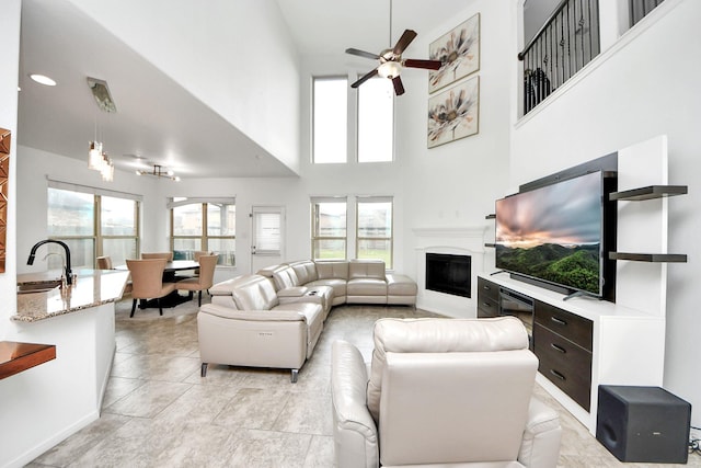 living room featuring a ceiling fan, a high ceiling, and a glass covered fireplace