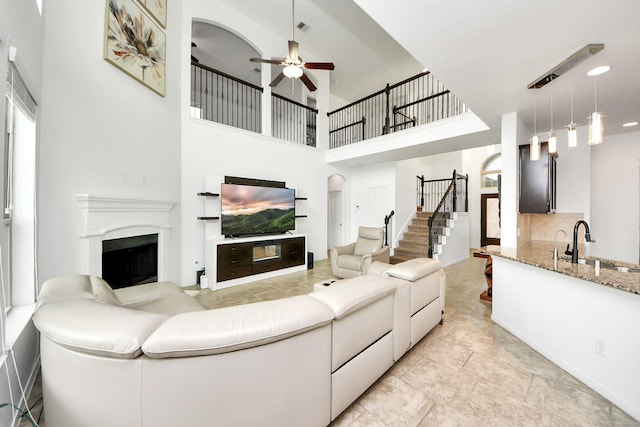 living area featuring ceiling fan, a fireplace, arched walkways, a towering ceiling, and stairway