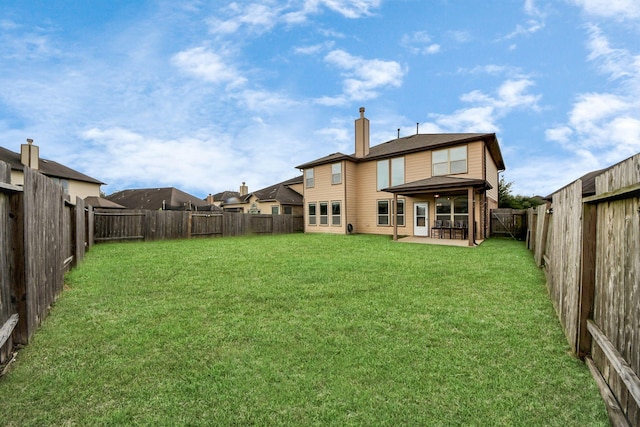 rear view of property with a yard, a chimney, a fenced backyard, and a patio area