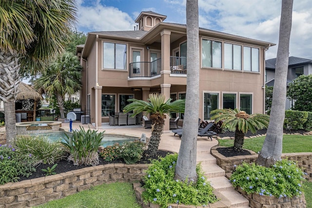 back of property featuring fence, a pool with connected hot tub, stucco siding, a patio area, and a balcony