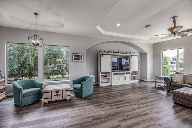 living area featuring arched walkways, a raised ceiling, and a healthy amount of sunlight