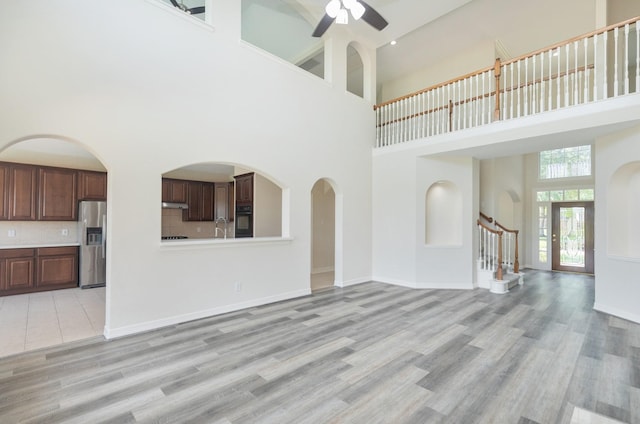 unfurnished living room with light wood-style floors, a ceiling fan, baseboards, and a towering ceiling